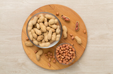 Peeled and unpeeled peanuts on wooden background, top view