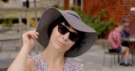Close-up portrait of woman in wide-brimmed hat and sunglasses, striking pose while looking into...
