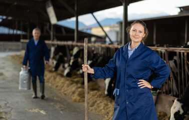 Obraz na płótnie Canvas Portrait of cheerful woman working on farm breeding Holstein dairy cows posing in cowshed..