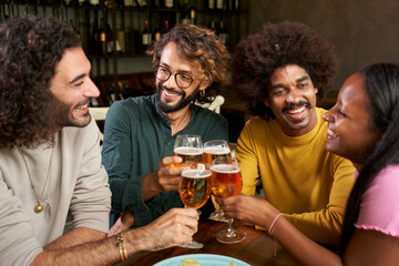 Group of young people having fun and drink beer in a bar toasting. This four multi-ethnic friends...