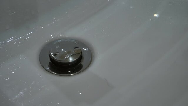Close-up of water from a faulty faucet dripping into a sink with a drain plug. Outdated plumbing, broken faucet, leaking. Drinking water shortage