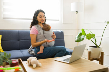 Beautiful mother doing remote work with a baby carrier