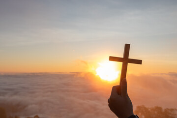 Human hand holding a crucifix praying to the GOD with bright sunbeam on the sky