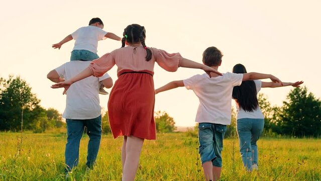 Joyful family, raising their hands, runs towards sun, dreams of flying in natural park, sunset. Slow motion. Family, mom dad and children play together, happy childhood. Happy people, children future