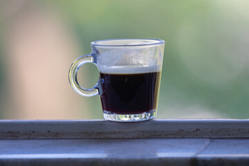 Transparent glass cup with black coffee on the window
