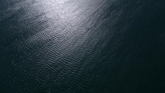 An aerial view of a majestic expanse of blue sea with lapping waves, the bright glint of the sun reflecting off the water