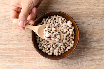 Black eye peas or cowpeas in bowl with spoon holding by hand on wooden background, Food ingredients, Table top view