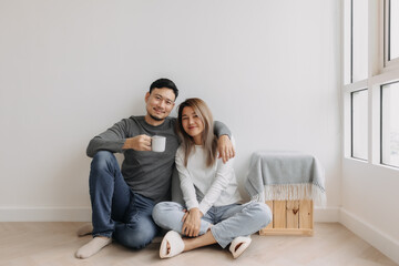 Happy romantic asian couple lover support with hug and coffee sit on the floor.