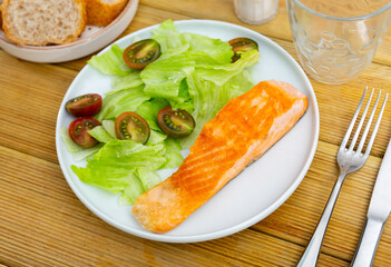 mediterranean cuisine.board table in plate narrow slice of fried salmon with green salad and cherry tomatoes, white bread