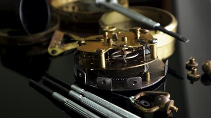 Antique disassembled and working table clock with obvious signs of dirt and aging next to various watchmaker's tools
