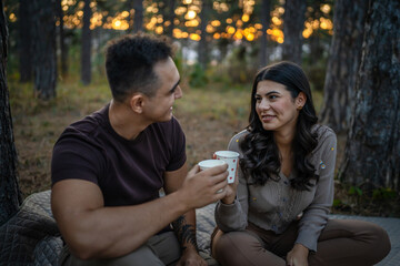 Young couple man and woman boyfriend and girlfriend or husband and wife in love relationship hold paper cup of coffee or tea while spend time together in the park forest bonding love real people