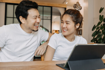 Happy laughing asian couple watching computer tablet together in the cafe.