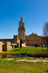 Fototapeta na wymiar View of tall Gothic bell tower of Cathedral in Burgo de Osma surrounded by ancient fortifications walls on sunny spring day. Historical religious monument of Spanish province of Soria