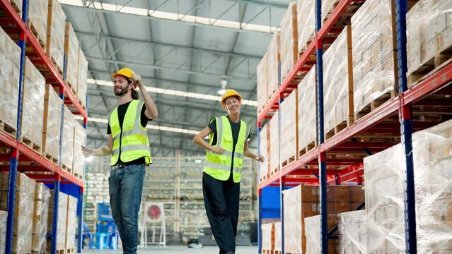 Young warehouse workers in uniform and helmet protective having fun and dancing in factory storehouse. Manual workers wearing vest and safety helmet having fun and happy relaxing in warehouse