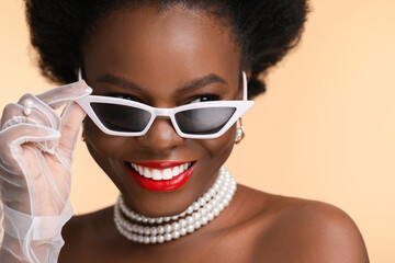 Fashionable portrait of beautiful happy woman with stylish sunglasses on beige background, closeup