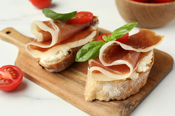 Tasty sandwiches with cured ham, basil and tomatoes on white table, closeup