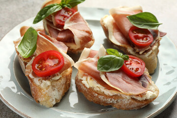 Tasty sandwiches with cured ham, basil and tomatoes on plate, closeup