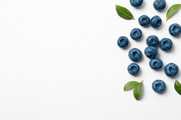 Tasty fresh blueberries with green leaves on white background, flat lay. Space for text