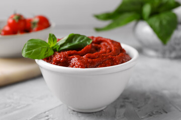 Tasty tomato paste and basil in bowl on light gray table, closeup