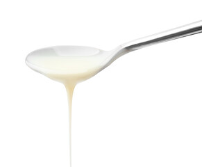 Pouring condensed milk from metal spoon isolated on white