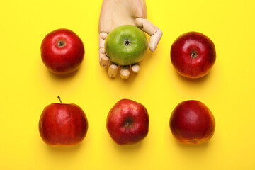 Mannequin hand with ripe red and green apples on yellow background, flat lay
