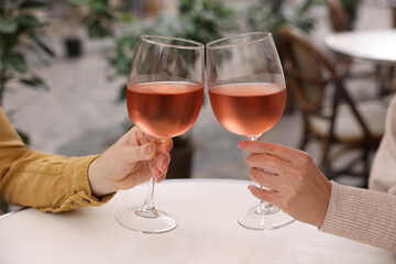 Women clinking glasses with rose wine at white table in outdoor cafe, closeup