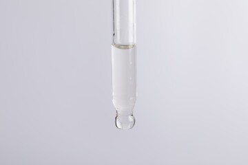 Dripping cosmetic serum from pipette on light grey background