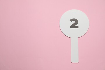 Auction paddle with number 2 on pink background, top view. Space for text