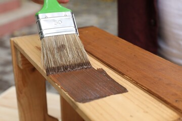 Man applying wood stain onto crate against blurred background, closeup