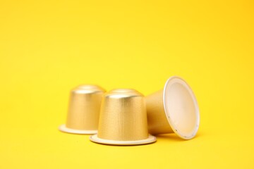 Three coffee capsules on yellow background, closeup