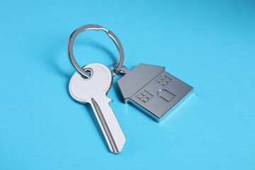 Key with keychain in shape of house on light blue background, closeup