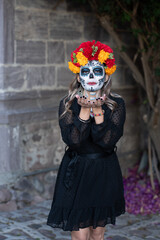 Fototapeta na wymiar Young woman with painted skull on her face for Mexico's Day of the Dead (El Dia de Muertos) against color background
