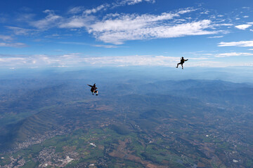 Two skydivers fly against the backdrop of a beautiful landscape
