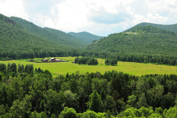 A huge clearing with a large farm surrounded by a fence at the foot of a high mountain with a dense...
