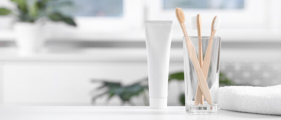 Bamboo toothbrushes in holder, toothpaste and towel on white table indoors, space for text. Banner design