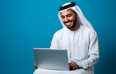 Happy young Arabic man isolated on a blue background, using a laptop device,