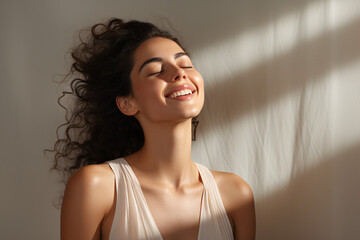 Young woman smiling with eyes closed, and head tilted up. Breathing deeply and feeling the light that touches her face. Chiaroscuro lighting. Expression of pleasant calm on her face..