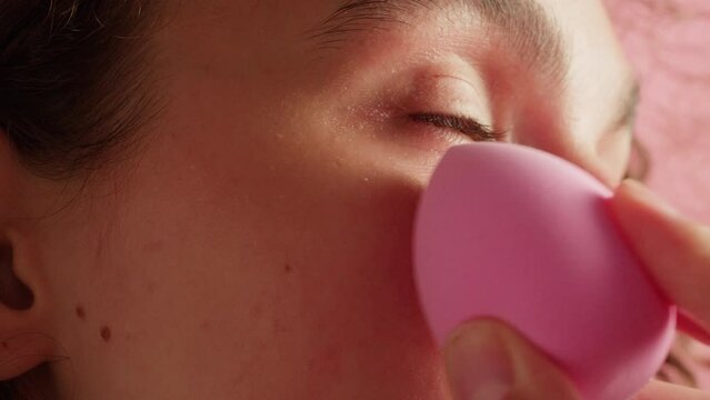 Beauty shot of woman applying foundation bb cream with sponge on previously applied moisturizing face lotion and smiling in camera. Concept of skincare, cosmetics, make up, beauty