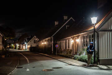 Bastad, Sweden A man stands under a street lamp  among old cottages  at night on the landmark and picturesque Agardhsgatan.