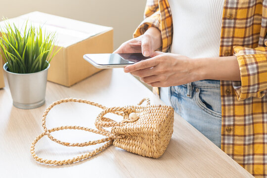 Online seller store, small business entrepreneur asian young woman using smart mobile phone taking photo bag or product with digital camera for promotion advertising sell post on internet market web.