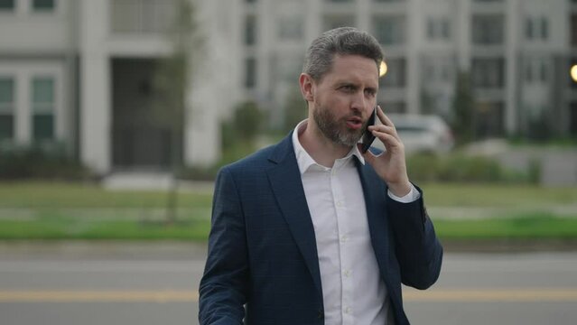 Portrait of a confident business man walking on street and speaking phone. Mature business man talking on phone outdoor. Businessman in a formal suit using phone.