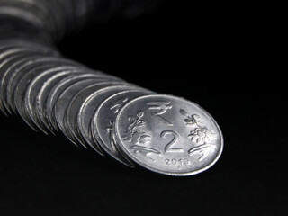 closeup shot of silver 2 (two) rupee indian coins arranged and stacked in a snake like curved row isolated in a black background