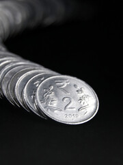 closeup shot of silver two rupee indian coins arranged and stacked in a snake like curved row isolated in a black background