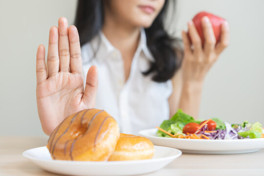 Diet, dieting, happy asian young woman, girl hand push out, deny sweet donut, doughnut on plate, choose red apple and green vegetable salad, eat food for good healthy, female getting weight loss.