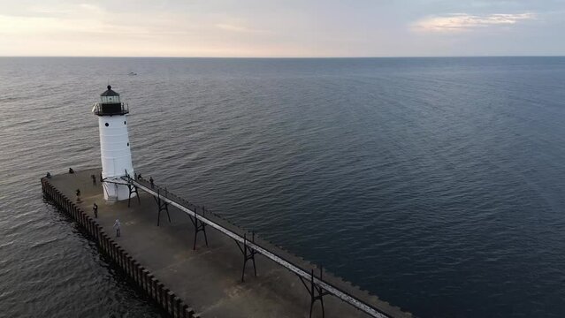 Manistee lighthouse on Lake Michigan. Aerial flyover shot crosses the catwalk towards the lake with the lighthouse to the side. Shot at dusk with a cloudy sky.