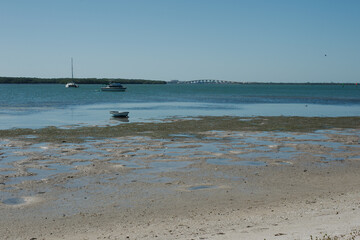 Maximo Beach Park bay water in St. Petersburg, FL. Sailboat no mast with a birds in water in front of the boat..  Looking south from the beach with sand, birds and water reflections.  Sunny blue sky w