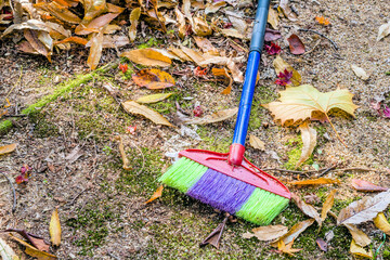 Colorful broom made of plastic laying on ground in nature park.