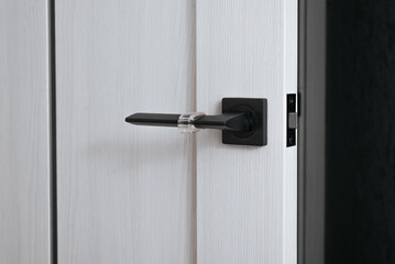 Close-up of a metal handle with a stopper and a lock in a white wooden open door