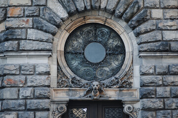 A round window with bars on the facade of an old house in Lviv. Head of a lion and fragment of a doorway.