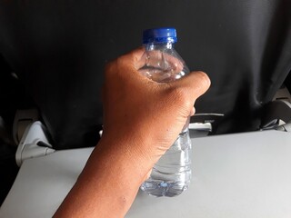 selective focus hand holding mineral water bottle above airplane flight cabin desk